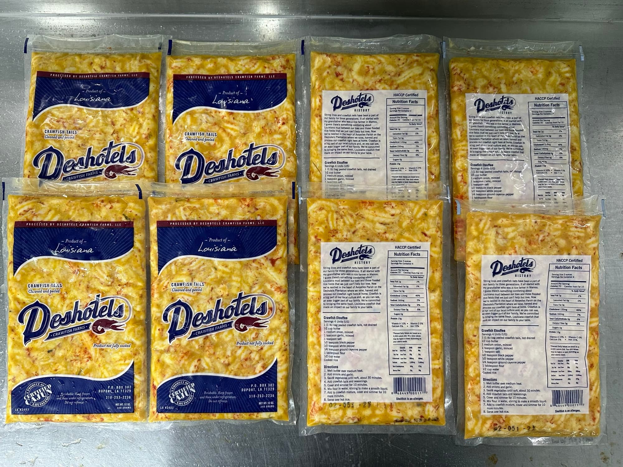 A flat-lay of Deshotels Crawfish Farms crawfish tail meat packages, a Ju's Crawfish Company brand, showing front labels and nutrition panels on a stainless surface